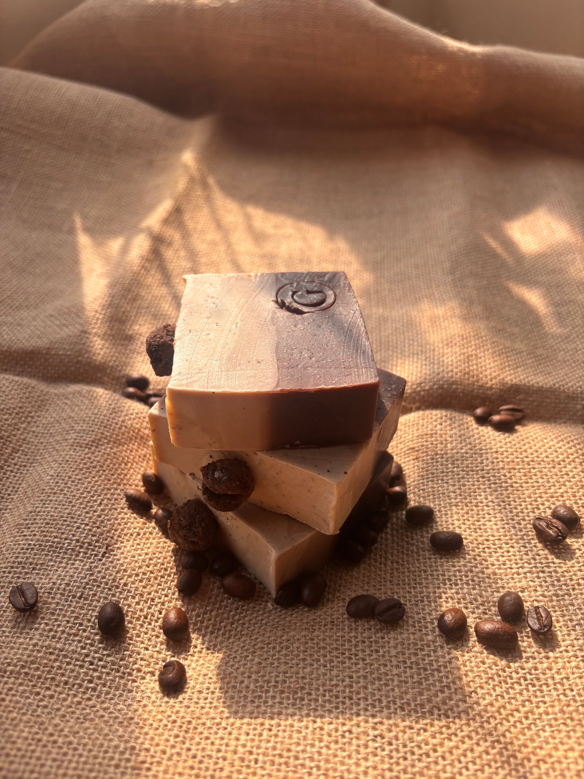 Image of artisanal handcrafted coffee soaps on a sunkissed window. The are of a gradient brown and moisturising because of the strong decoction and moisturing kokum butter used. The Soaps are stamped with the logo of Gaia and You are natural wellness brand.